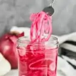 pickled red onions coming out of a mason jar with a fork