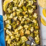 overhead view of roasted broccoli and cauliflower on a baking sheet garnished with lemon