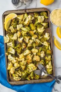 overhead view of roasted broccoli and cauliflower on a baking sheet garnished with lemon