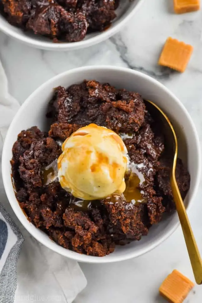 overhead view of bowl of crock pot brownies with a spoonful of vanilla ice cream and a drizzle of caramel 