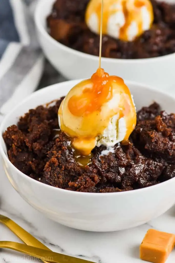 salted caramel crock pot brownies in a white bowl with ice cream and dripping caramel