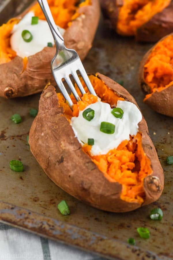 fork digging into a crock pot baked sweet potato with sour cream and green onions