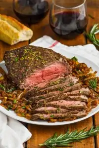 easy top round roast beef recipe garnished with fresh herbs and on a plate of caramelized onions