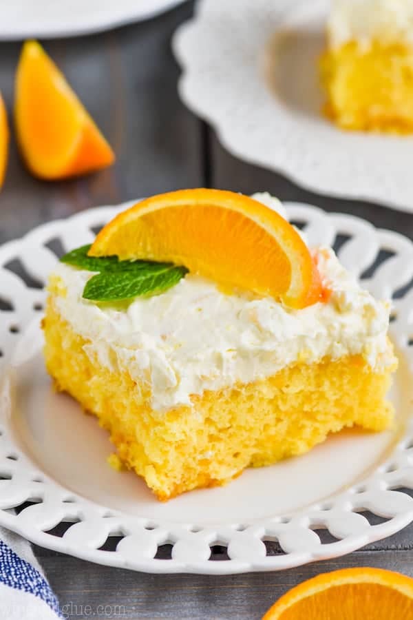 mandarin orange cake recipe on a white plate with a fluffy frosting on top with a slice of orange. 