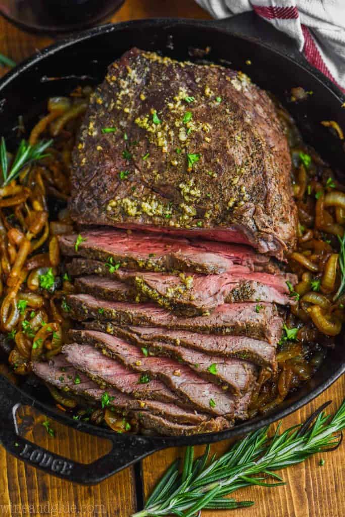 overhead view of sliced roast beef recipe in a cast iron skillet with caramelized onions