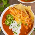 close up overhead view of a bowl of chicken tortilla soup recipe that has been garnished with sour cream, sliced jalapeños, shredded cheese, and tortilla chips
