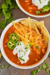 close up overhead view of a bowl of chicken tortilla soup recipe that has been garnished with sour cream, sliced jalapeños, shredded cheese, and tortilla chips