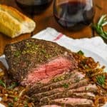 easy top round roast beef recipe garnished with fresh herbs and on a plate of caramelized onions