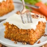 a fork sticking into a piece of carrot cake that is topped with cream cheese frosting