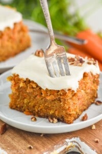 a fork sticking into a piece of carrot cake that is topped with cream cheese frosting