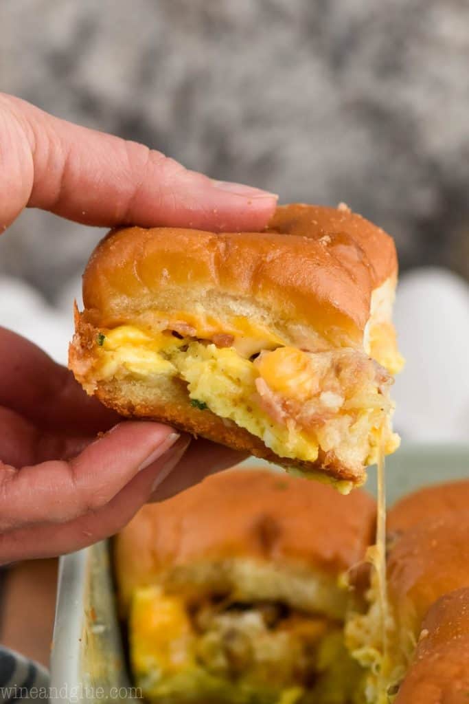 hand holding a breakfast slider sandwich over casserole dish