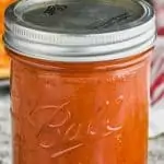 ball jar filled with homemade pizza sauce recipe surrounded by parsley leaves with pizza in the background