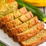 sliced loaf of Banana Zucchini Bread. Bananas and zucchini beside cutting board.