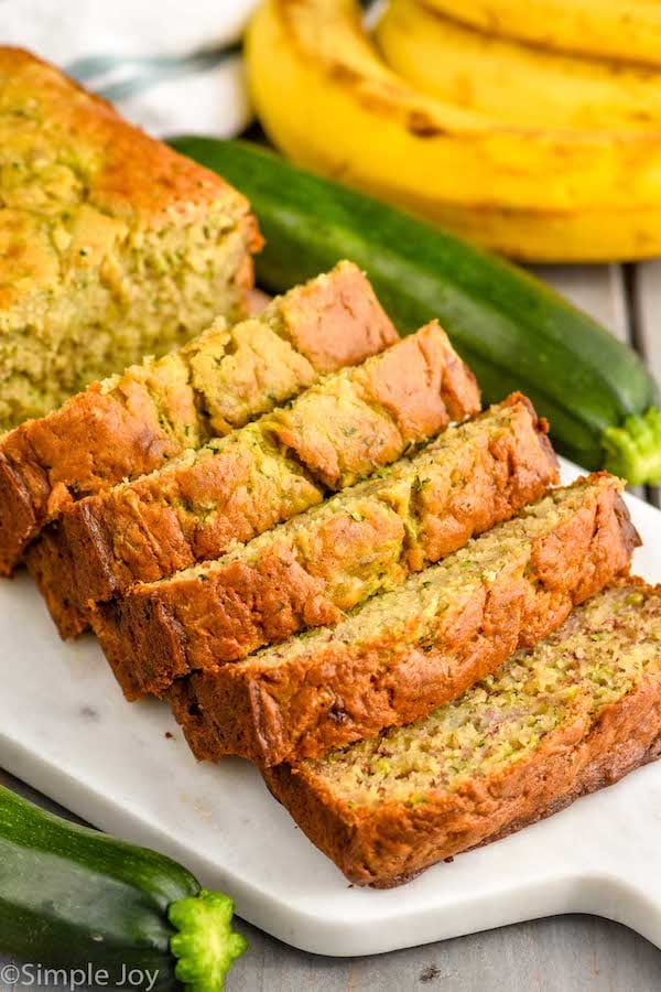 sliced loaf of Banana Zucchini Bread. Bananas and zucchini beside cutting board.