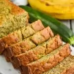 a side view of zucchini banana bread sliced on a marble cutting board with a zucchini and banana in the background