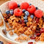 bowl of homemade granola with milk, a spoon, fresh raspberries and blueberries - 19