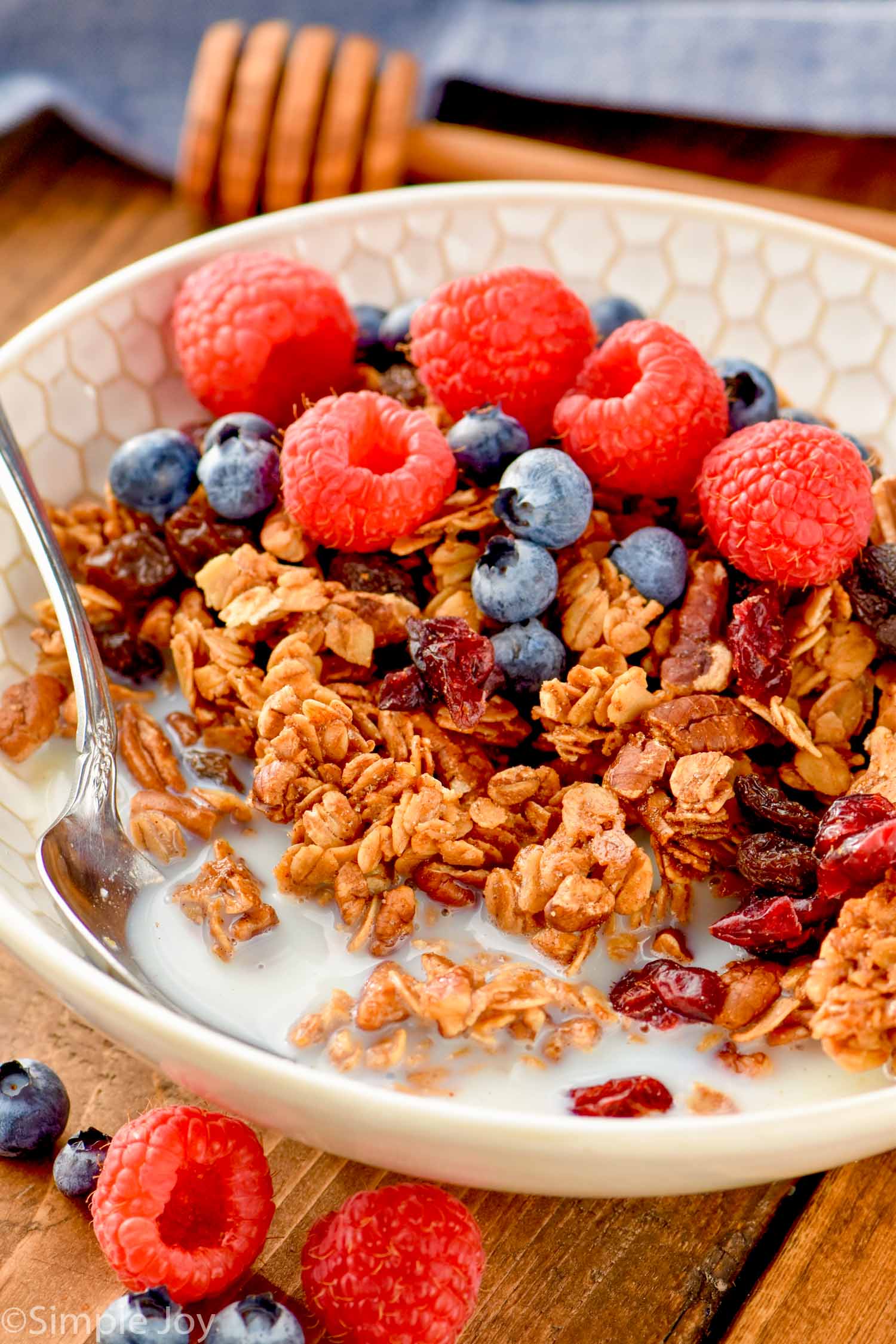 bowl of homemade granola with milk, a spoon, fresh raspberries and blueberries