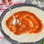 woman using a metal spoon to spread pizza sauce onto a circle pizza pan with dough on it - 13