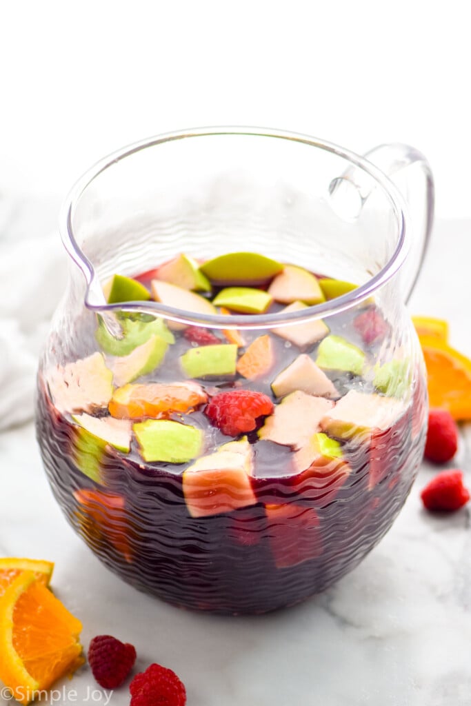 pitcher of red sangria with cut up apples, oranges, and raspberries