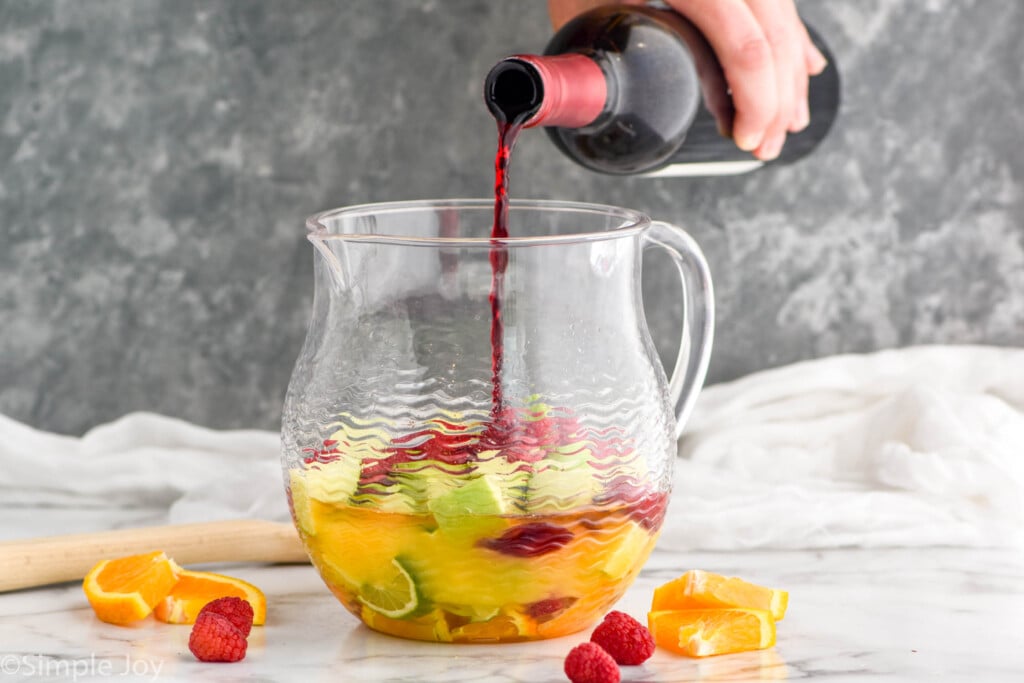 pouring a bottle of red wine in a pitcher that has fruit and orange juice