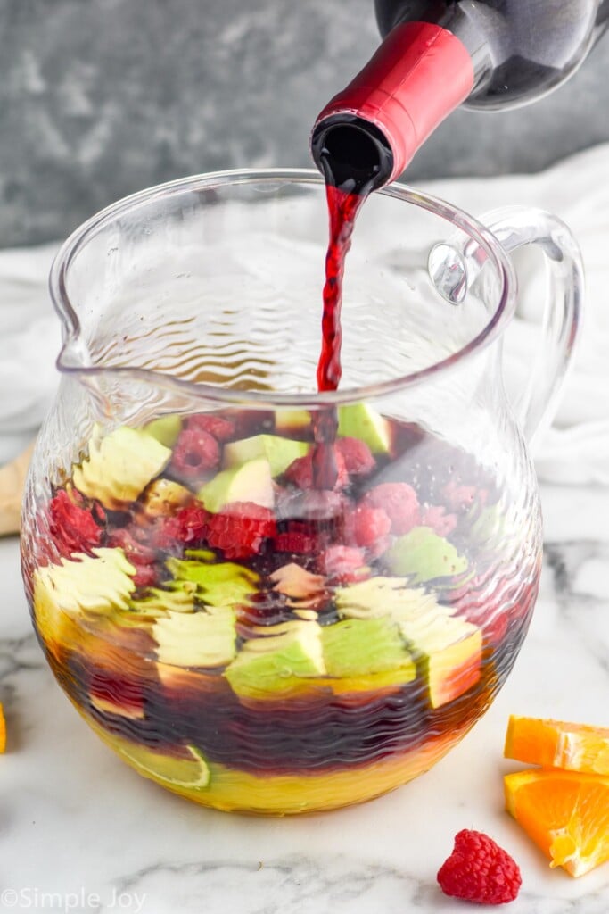 close up of pouring wine in a pitcher with fruit and orange juice to make red wine sangria recipe