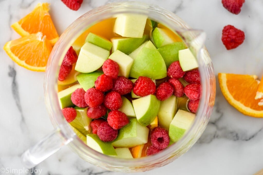 overhead of fruit in a pitcher cut up - apples, oranges, and raspberries, to make red sangria