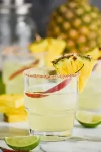 tumbler glass filled with spicy pineapple margarita and garnished with a chile pepper and a slice of pineapple