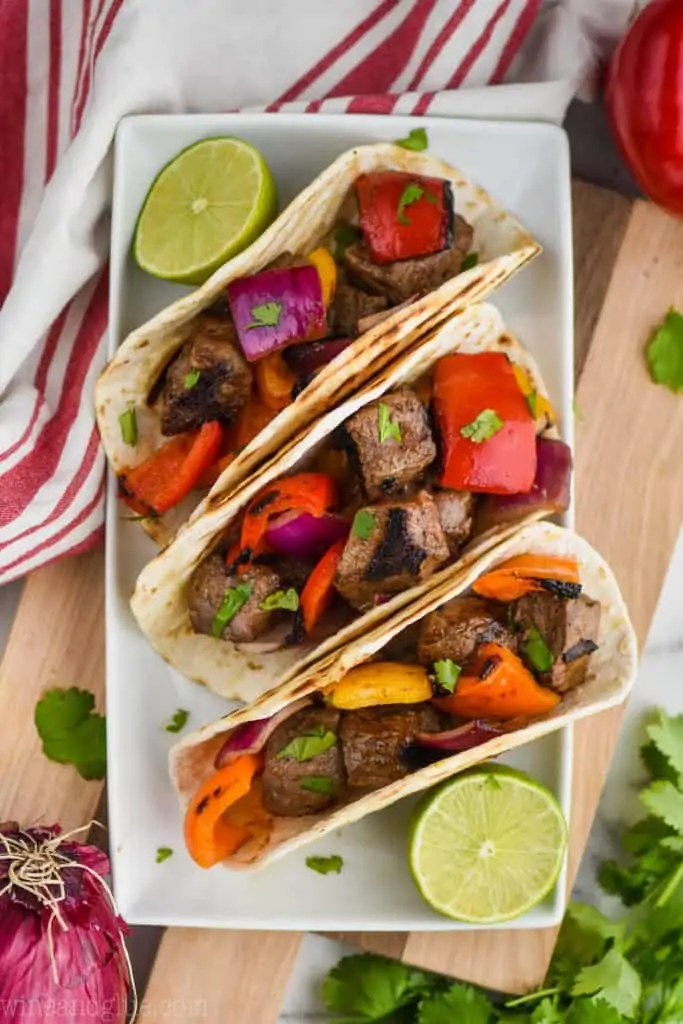 overhead of three steak fajitas on a white plate with a cut lime