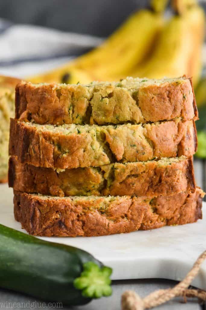 stack of slices of the best zucchini banana bread recipe on a marble cutting board with a zucchini in front and a banana bunch in the back