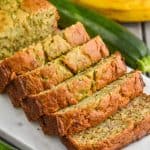 a side view of zucchini banana bread sliced on a marble cutting board with a zucchini and banana in the background