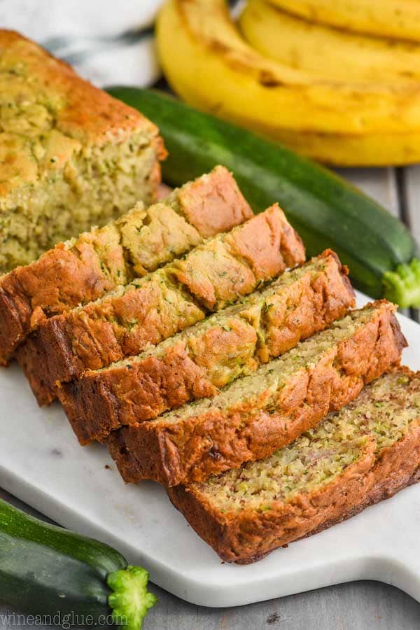 a side view of zucchini banana bread sliced on a marble cutting board with a zucchini and banana in the background