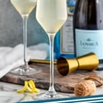 Pinterest graphic for French 75 recipe. Image is photo of two French 75 cocktails garnished with lemon peels. Bottles of gin and champagne are in the background. Text says, "The Best French 75 simplejoy.com."