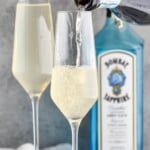 Pinterest graphic for French 75 recipe. Text says, "The Best French 75 simplejoy.com." Image is photo of champagne being poured into champagne flute for French 75 recipe with a bottle of gin in the background.