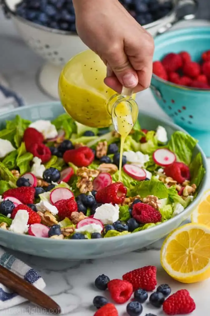woman pouring lemon poppy seed dressing on a simple summer salad recipe
