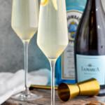 Photo of two French 75 cocktails. Bottles of gin and champagne for cocktail are behind the cocktails. - 9