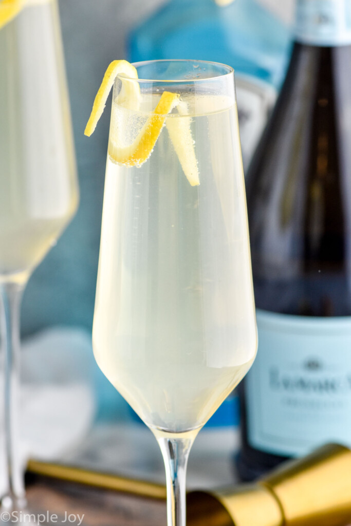 Close up photo of French 75 cocktail. Bottles of gin and champagne are behind cocktail.