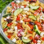 clear bowl with rotini noodles, vegetables, and feta cheese for a greek pasta salad recipe - 9