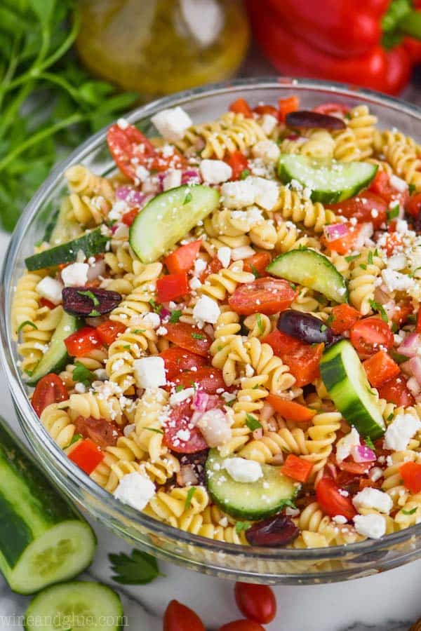 clear bowl with rotini noodles, vegetables, and feta cheese for a greek pasta salad recipe