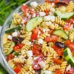 clear bowl with rotini noodles, vegetables, and feta cheese for a greek pasta salad recipe