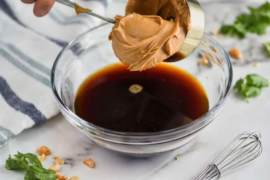 creamy peanut butter being put into a bowl filled with apple cider vinegar and soy sauce - 5