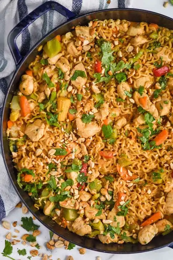 overhead view of peanut butter stir fry noodles in a large skillet, topped with fresh cilantro and chopped peanuts