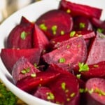 a white bowl on a wood mat filled with wedges of roasted beets sprinkled with parsley - 19
