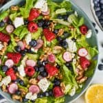 overhead view of a summer salad recipe with fresh raspberries, blueberries, radishes, romain lettuce, walnuts, and goat cheese all with a lemon poppyseed dressing in a big blue bowl