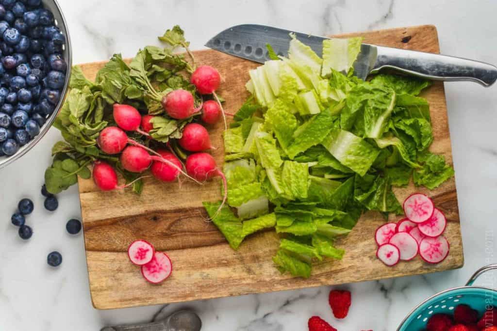 ingredients for a fast summer salad recipe on a wood chopping board: radishes, romain lettuce, blueberries, and raspberries