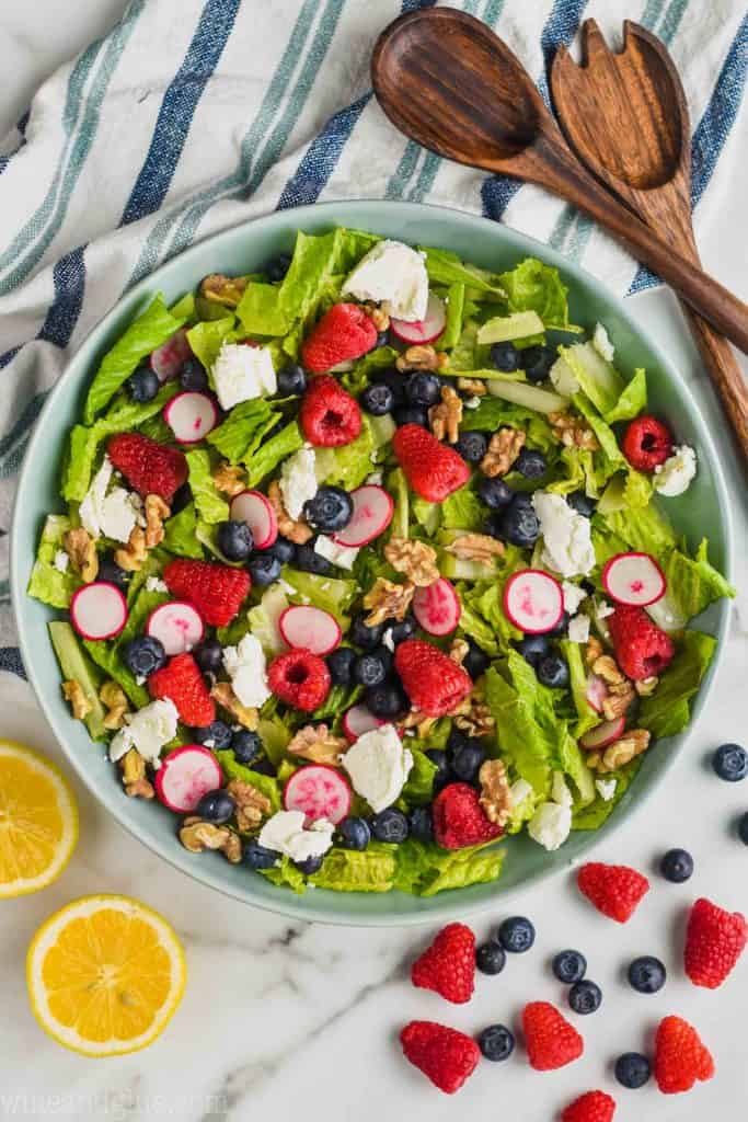 overhead view of easy summer salad recipe with raspberries, blueberries, goat cheese, walnuts, radishes, and romain lettuce in a big blue bowl