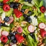 overhead view of a summer salad recipe with fresh raspberries, blueberries, radishes, romain lettuce, walnuts, and goat cheese all with a lemon poppyseed dressing in a big blue bowl