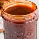 up close of bbq sauce recipe in a wide mouth ball jar with it dripping down the side and grilled bbq chicken in the background