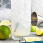 pinterest graphic of a tall glass with ice filled with a gin rickey, garnished with a lime wedge and with a metal straw, says "low calorie gin rickey simplejoy.com"