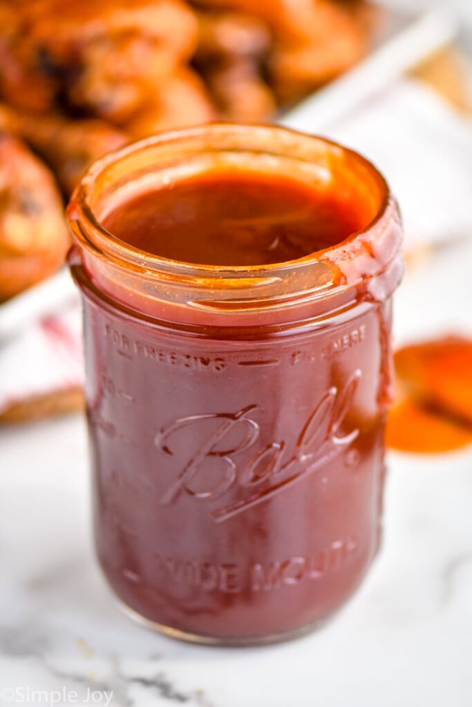 up close of bbq sauce recipe in a wide mouth ball jar with it dripping down the side and grilled bbq chicken in the background