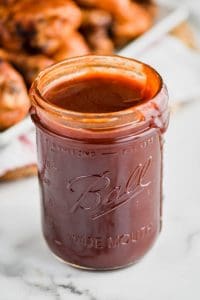 up close of bbq sauce recipe in a wide mouth ball jar with it dripping down the side and grilled bbq chicken in the background